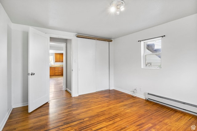 unfurnished bedroom featuring wood finished floors, a baseboard heating unit, baseboards, and multiple windows