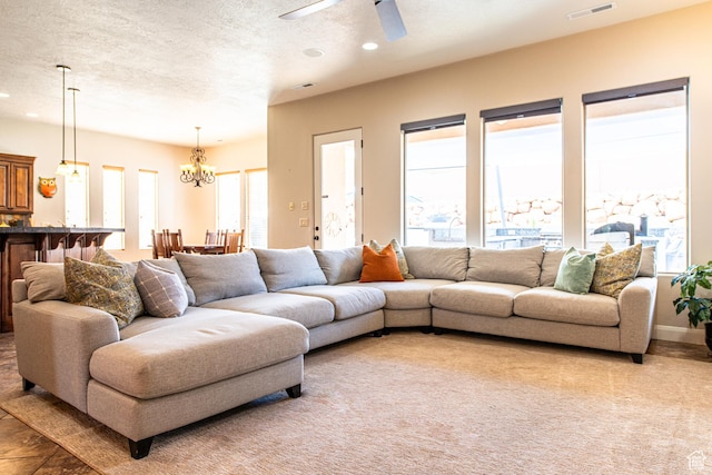 living room with a textured ceiling, ceiling fan with notable chandelier, visible vents, and recessed lighting