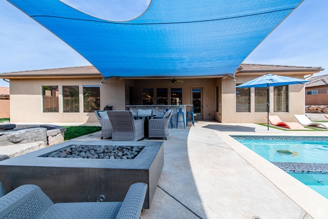 back of property featuring a fenced in pool, a patio, stucco siding, outdoor dry bar, and a fire pit