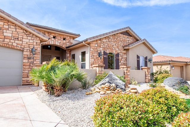 mediterranean / spanish home featuring an attached garage, driveway, stucco siding, and stone siding