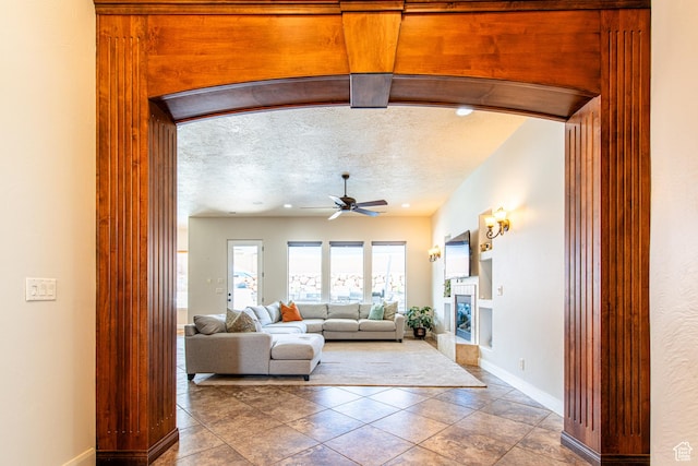 tiled living room featuring baseboards, a ceiling fan, and a glass covered fireplace
