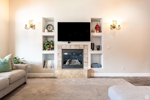 carpeted living room featuring baseboards, a tile fireplace, and built in shelves