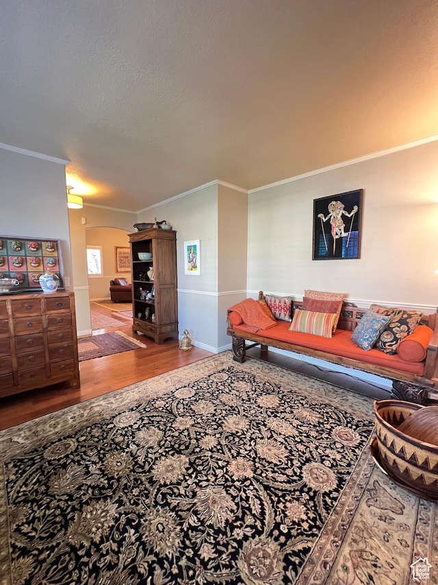 living area with a textured ceiling, wood finished floors, baseboards, and ornamental molding