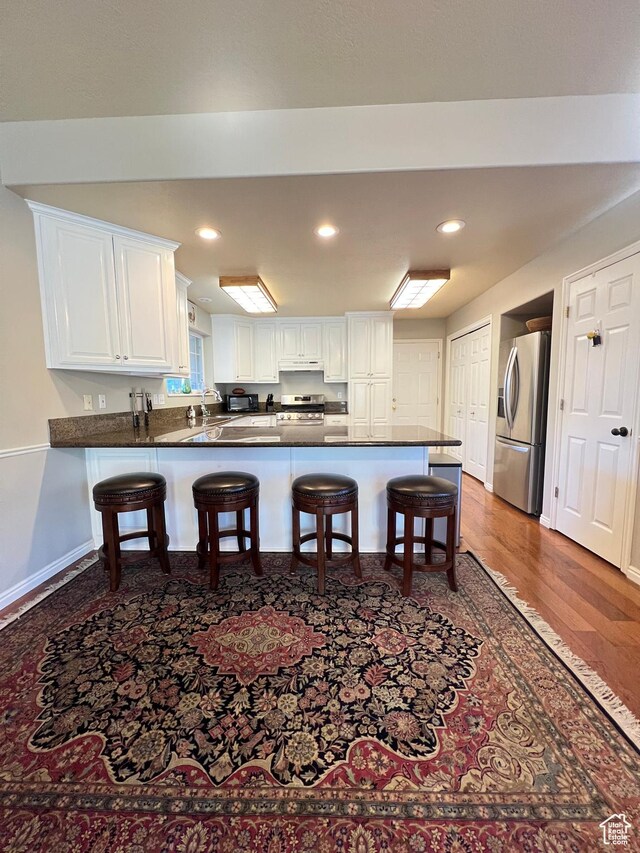 kitchen with white cabinets, dark countertops, a peninsula, under cabinet range hood, and stainless steel appliances