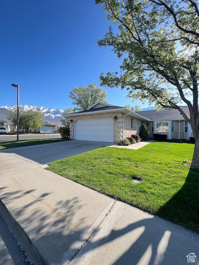 ranch-style home featuring a mountain view, an attached garage, concrete driveway, brick siding, and a front lawn