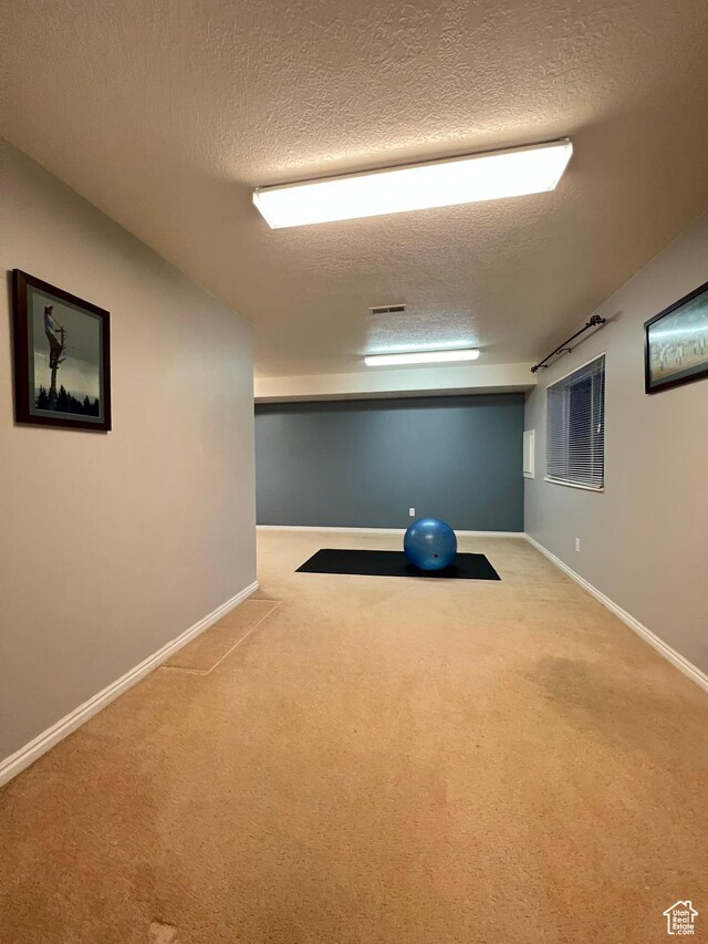 exercise area featuring carpet flooring, visible vents, a textured ceiling, and baseboards
