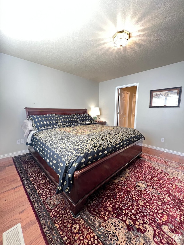 bedroom with a textured ceiling, baseboards, and wood finished floors