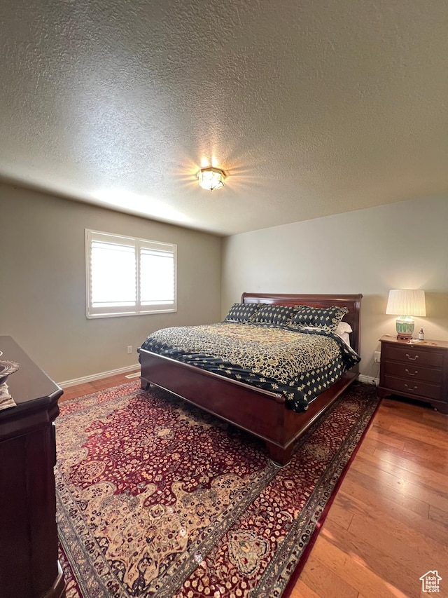 bedroom featuring wood-type flooring, baseboards, and a textured ceiling