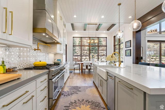 kitchen with high end stove, wall chimney range hood, a chandelier, a sink, and light wood finished floors