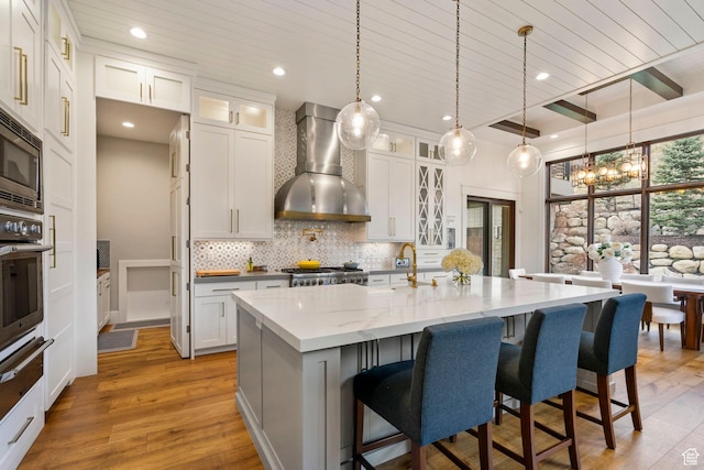 kitchen with pendant lighting, tasteful backsplash, light wood-type flooring, wall chimney range hood, and stainless steel appliances