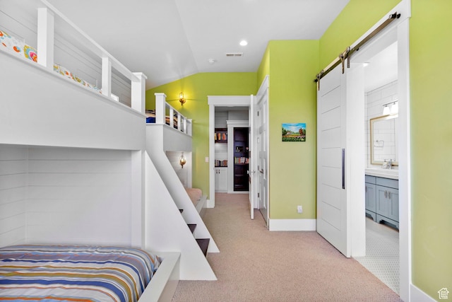 carpeted bedroom featuring visible vents, baseboards, vaulted ceiling, and a barn door