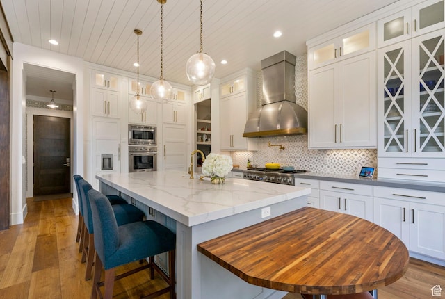 kitchen with stainless steel appliances, white cabinets, decorative backsplash, and wall chimney range hood