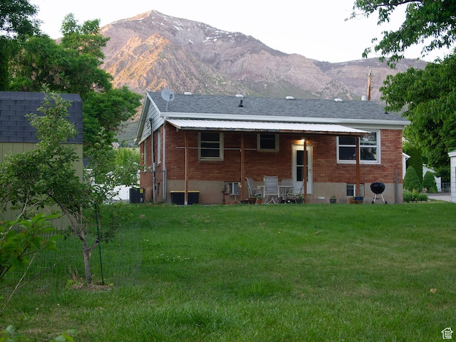 back of property with roof with shingles, a yard, a mountain view, and brick siding