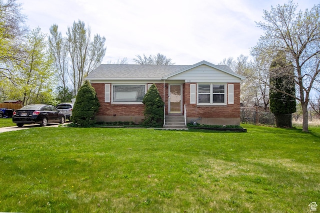 view of front facade with entry steps, fence, a front lawn, and brick siding