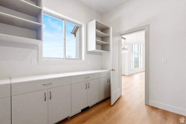 kitchen with baseboards, open shelves, light countertops, light wood-type flooring, and a chandelier