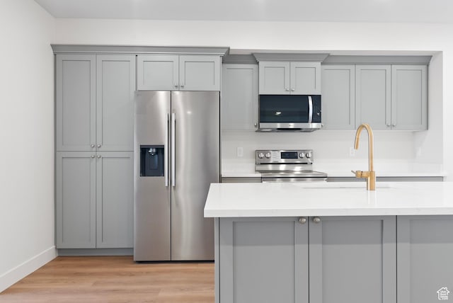 kitchen with baseboards, light wood-type flooring, gray cabinets, appliances with stainless steel finishes, and a sink
