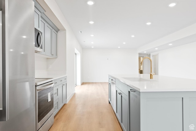 kitchen with a sink, freestanding refrigerator, stainless steel microwave, gray cabinetry, and range