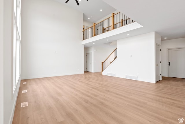 unfurnished living room featuring light wood-style floors, a ceiling fan, visible vents, and stairway
