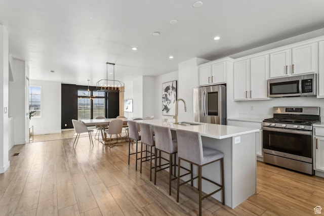 kitchen with a sink, light countertops, appliances with stainless steel finishes, an island with sink, and a chandelier