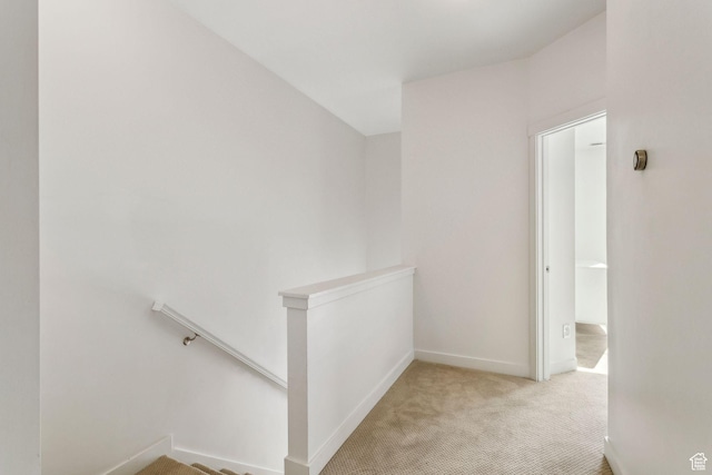 hallway with baseboards, an upstairs landing, and light colored carpet
