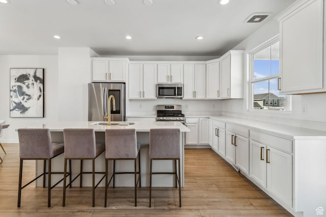 kitchen with white cabinets, appliances with stainless steel finishes, a kitchen island with sink, light countertops, and a sink