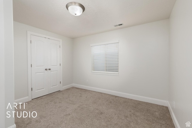 unfurnished room with carpet, visible vents, baseboards, and a textured ceiling