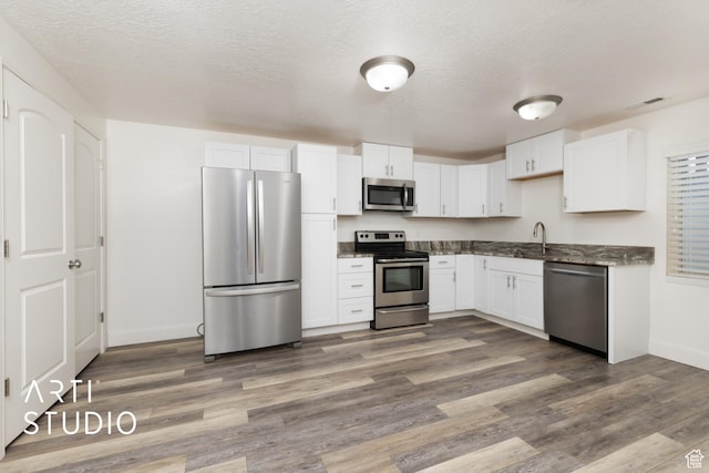 kitchen featuring white cabinetry, baseboards, appliances with stainless steel finishes, and wood finished floors