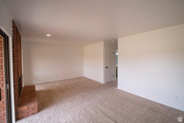 carpeted empty room with a brick fireplace and recessed lighting