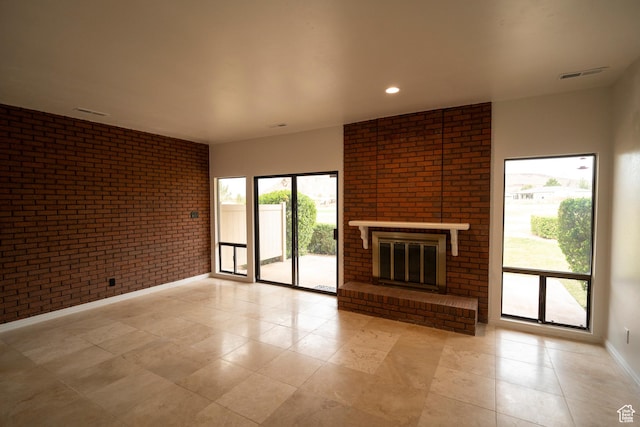 unfurnished living room featuring visible vents, light tile patterned flooring, a brick fireplace, brick wall, and baseboards