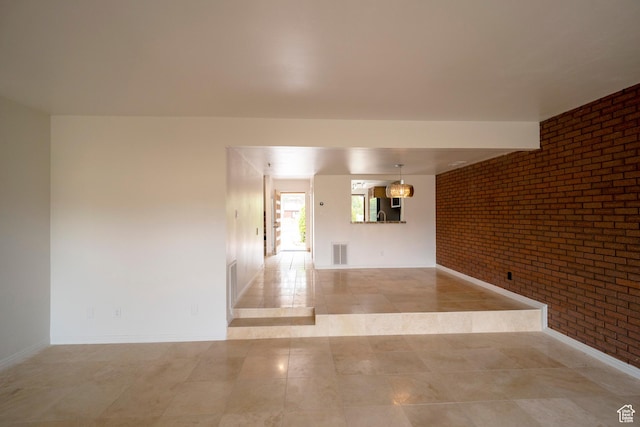 tiled spare room featuring visible vents, baseboards, and brick wall