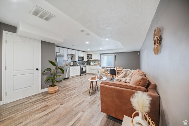 living room featuring light wood-style floors, baseboards, visible vents, and recessed lighting