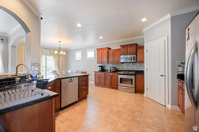 kitchen with tasteful backsplash, dark countertops, a chandelier, crown molding, and stainless steel appliances