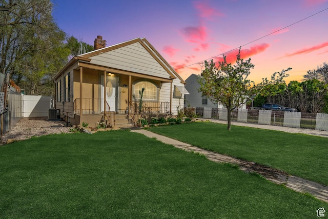 bungalow-style house featuring central AC unit, a yard, covered porch, a chimney, and fence private yard