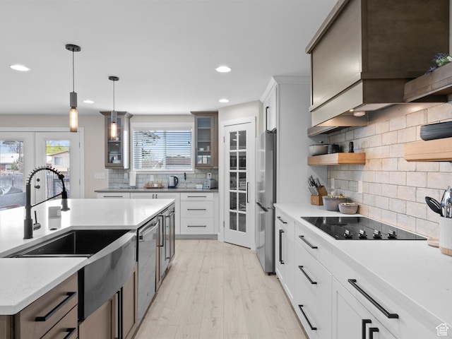 kitchen featuring glass insert cabinets, a sink, appliances with stainless steel finishes, light wood finished floors, and decorative backsplash