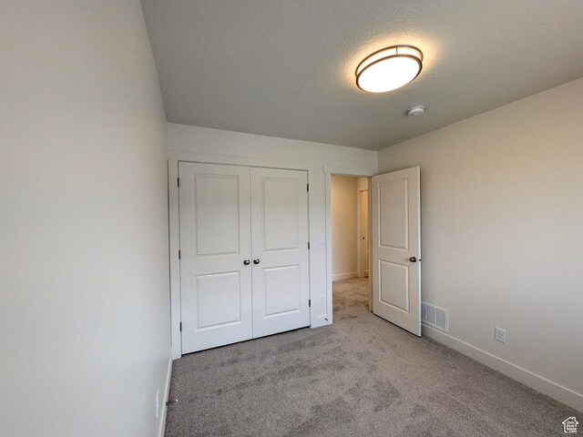 unfurnished bedroom featuring a closet, baseboards, a textured ceiling, visible vents, and carpet