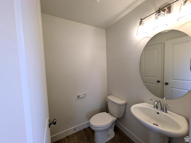 half bathroom with baseboards, a sink, toilet, a textured ceiling, and wood finished floors