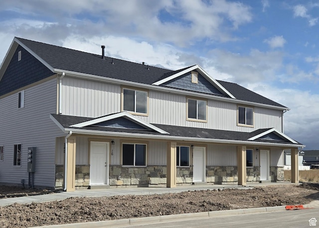view of front of property with a porch, stone siding, and roof with shingles