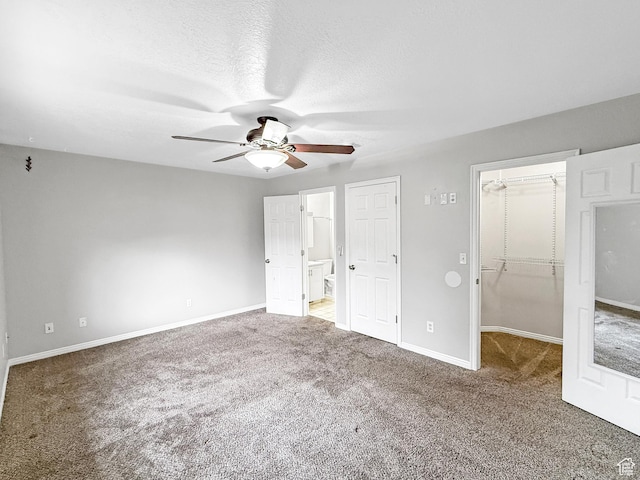 unfurnished bedroom featuring a closet, baseboards, ceiling fan, carpet, and a walk in closet