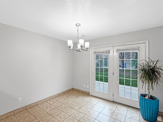 unfurnished dining area with a notable chandelier, baseboards, a textured ceiling, light tile patterned flooring, and visible vents