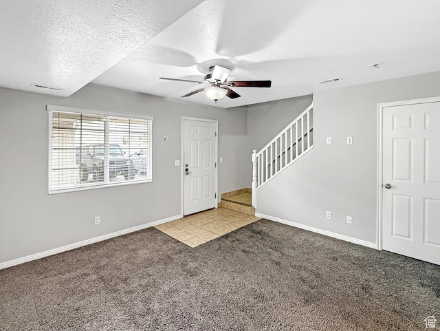 tiled foyer with baseboards, stairway, carpet floors, visible vents, and ceiling fan