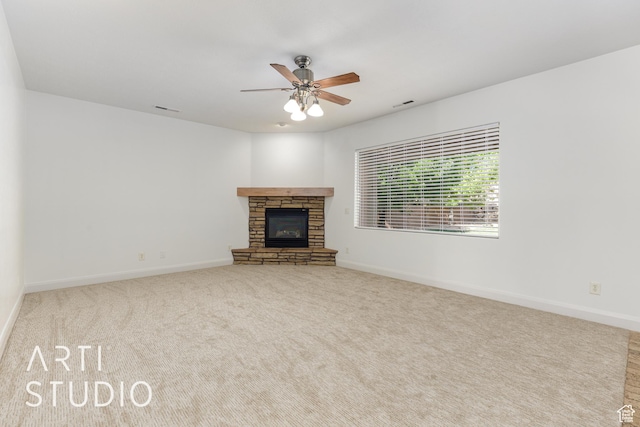 unfurnished living room featuring baseboards, a ceiling fan, a stone fireplace, and carpet floors