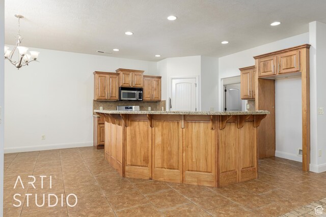 kitchen with recessed lighting, light stone countertops, stainless steel microwave, brown cabinets, and a kitchen breakfast bar