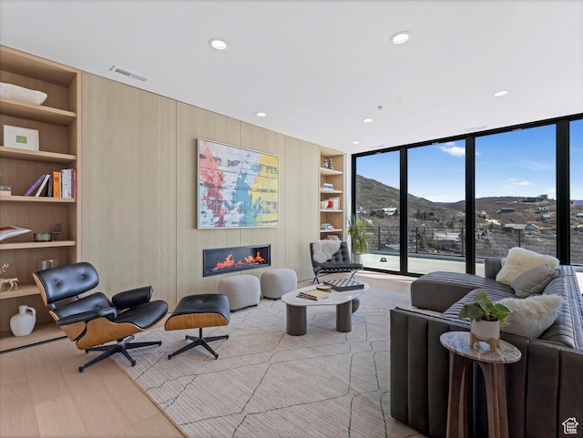 living room featuring built in shelves, a glass covered fireplace, recessed lighting, and wood finished floors
