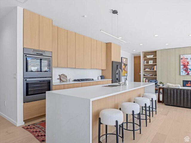 kitchen featuring stainless steel appliances, modern cabinets, light brown cabinetry, light wood-type flooring, and a breakfast bar