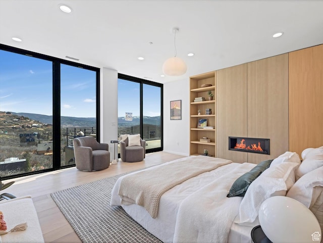 bedroom with floor to ceiling windows, light wood finished floors, a large fireplace, recessed lighting, and a mountain view