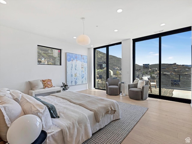bedroom with a wall of windows, access to exterior, wood finished floors, and recessed lighting