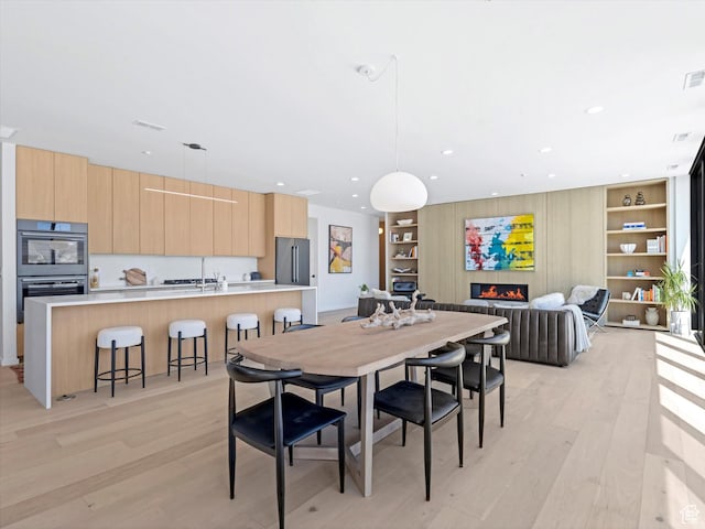 dining room featuring light wood-style floors, a lit fireplace, built in shelves, and recessed lighting