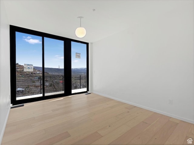 unfurnished room featuring light wood finished floors, floor to ceiling windows, and baseboards