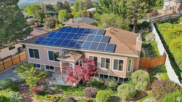 3391 E Brockbank Dr S, Millcreek, UT 84124 - rear view of property featuring roof mounted solar panels, a chimney, a fenced backyard, stucco siding, and roof with shingles