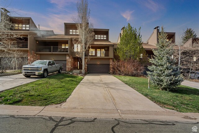 view of front of property featuring an attached garage, concrete driveway, a front lawn, and a balcony